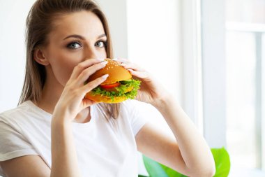 Genç bir kadın yağlı burger yiyor, kilo verme konsepti..