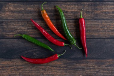 Red and green chili peppers on a black plat on a wooden table.