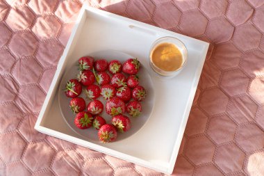 Yatakta servis edilen taze çilekli bir bardakta kahve.