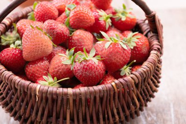 Taze olgun çilekler hasır sepetin içinde beyaz kırsal masada.