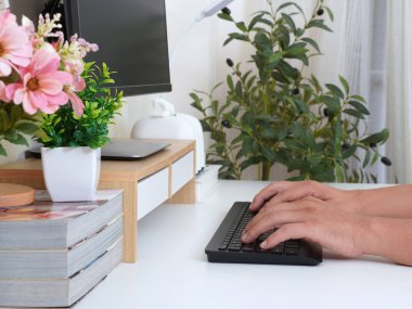 Bilgisayar, dizüstü bilgisayar, dergiler ve saksı bitkileriyle çevrili, elleri klavyede yazan modern çalışma alanı. Üretkenlik ve yaratıcılık için parlak ve temiz bir ortam..