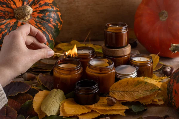 light soy candles burn in glass jars. Tree leaves, pumpkin. Comfort at home. Candle in a brown jar. Scent and light. Scented handmade candle. Aroma therapy. Autumn mood. Cozy home decor in fall.