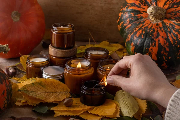 light soy candles burn in glass jars. Tree leaves, pumpkin. Comfort at home. Candle in a brown jar. Scent and light. Scented handmade candle. Aroma therapy. Autumn mood. Cozy home decor in fall.