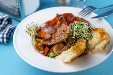 Biftek, sebze, kızarmış ekmek ve mikroyeşil salata. Restoran masasının üstünde. Kasede et yemeği. Pirzola, madalyon, pirzola. Mavi arkaplan, yakın plan