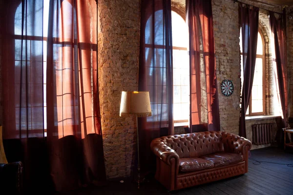 Windows at empty Library room with a brick wall. Leather sofa in a vintage style. The furniture in the room. Dark brown interior.
