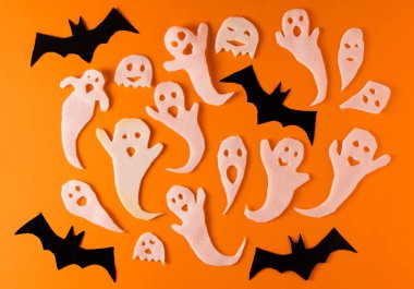 White ghosts and bat craft for Halloween party. Wrapping paper ghost on orange background top view. Cartoon creepy Whisper. DIY hand made. Set boo characters.