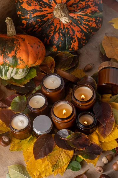 Soy candles burn in glass jars. Tree leaves, pumpkin. Comfort at home. Candle in a brown jar. Scent and light. Scented handmade candle. Aroma therapy. Autumn mood. Cozy home decor in fall.