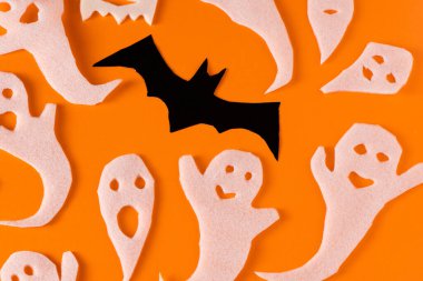 White ghosts and bat craft for Halloween party. Wrapping paper ghost on orange background top view. Cartoon creepy Whisper. DIY hand made. Set boo characters.