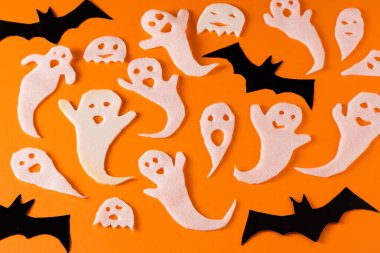 White ghosts and bat craft for Halloween party. Wrapping paper ghost on orange background top view. Cartoon creepy Whisper. DIY hand made. Set boo characters.