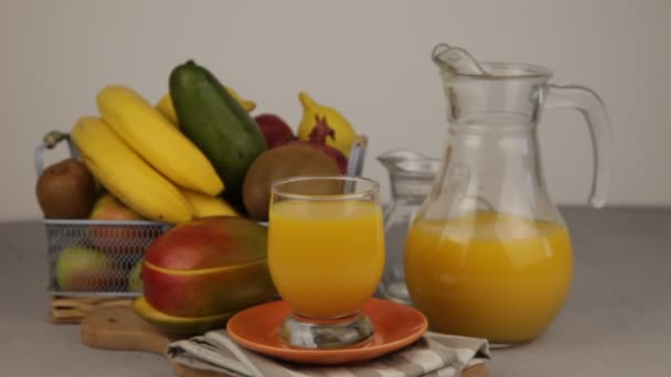 黄色のさわやかな夏の飲み物 新鮮なマンゴージュース オレンジジュース テーブルの上にフルーツバスケット ジュースのグラスだ キッチンで新鮮な果物やジュース ビーガンフード ビタミンドリンク バナナ キウイ — ストック動画