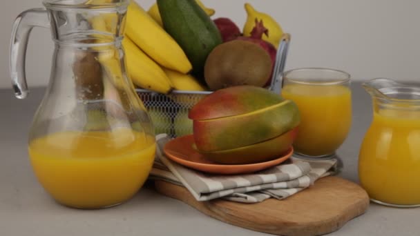 黄色のさわやかな夏の飲み物 新鮮なマンゴージュース オレンジジュース テーブルの上にフルーツバスケット ジュースのグラスだ キッチンで新鮮な果物やジュース ビーガンフード ビタミンドリンク バナナ キウイ — ストック動画