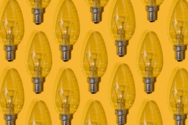 Yellow background. Electric light bulbs pattern. An old glass electric light bulb with a tungsten filament. The concept of electricity consumption and saving. Obsolete energy.