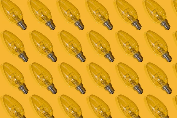 Yellow background. Electric light bulbs pattern. An old glass electric light bulb with a tungsten filament. The concept of electricity consumption and saving. Obsolete energy.