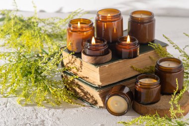 A set of different aroma candles in brown glass jars. Scented handmade candle. Soy candles are burning in a jar. Aromatherapy and relax in spa and home. Fire in brown jar. Yellow flowers