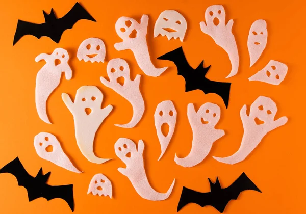 White ghosts and bat craft for Halloween party. Wrapping paper ghost on orange background top view. Cartoon creepy Whisper. DIY hand made. Set boo characters.