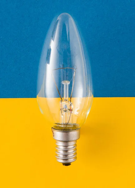 An old glass electric light bulb with a tungsten filament. The concept of electricity consumption and saving. Obsolete energy. Light bulb on blue yellow background.