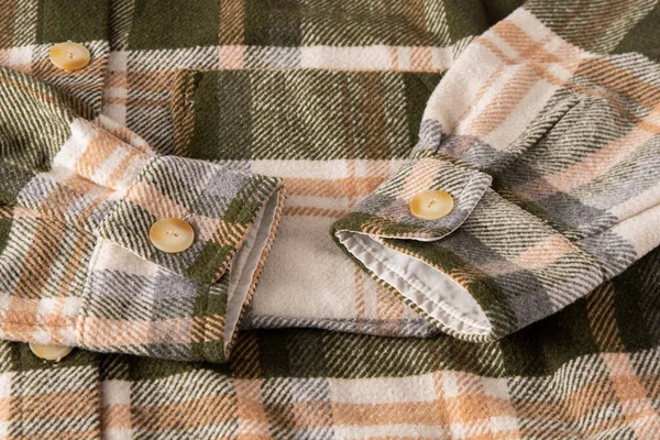 The sleeves and cuffs of the shirt are plaid. Clothing background large. Beige buttons. Unisex plaid shirt. Cuff on clothes. Green and brown color. Checkered shirt