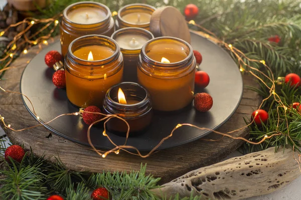 Soy candles burn in glass jars. Comfort at home. Candle in a brown jar. Scent and light. Scented handmade candle. Aroma therapy. Christmas tree and winter mood. Cozy decor. Festive garland decoration