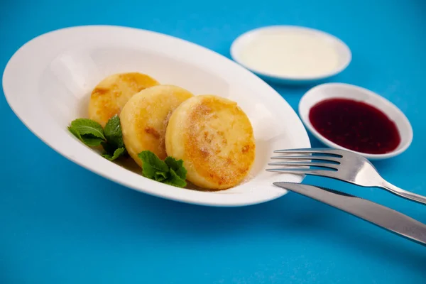 stock image Round cottage cheese pancakes in a white plate on a blue background. Food breakfast. Healthy food. Sour cream sauce and mint. Top view closeup. Dessert meal. Curd cheese pancake ricotta fritters.