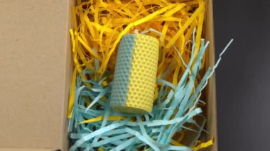 Yellow and blue beeswax candle comes in a gift box. Candle box with paper shavings. A product of beekeeping. Wax candle DIY. Bee honeycomb handmade craft. Top view. Aroma therapy. Romance decor.