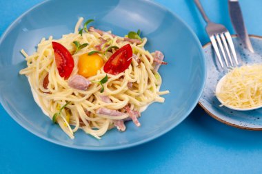 Peynirli ve yumurtalı makarna, pastırma ve domates, mikroyeşil. Mavi tabakta yemek. Ev yapımı carbonara makarnası. Öğle yemeği masanın üst tarafında. Jambonlu İtalyan spagettisi, krema.