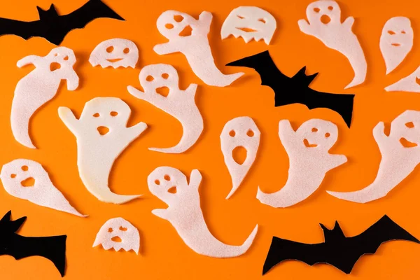 White ghosts and bat craft for Halloween party. Wrapping paper ghost on orange background top view. Cartoon creepy Whisper. DIY hand made. Set boo characters.