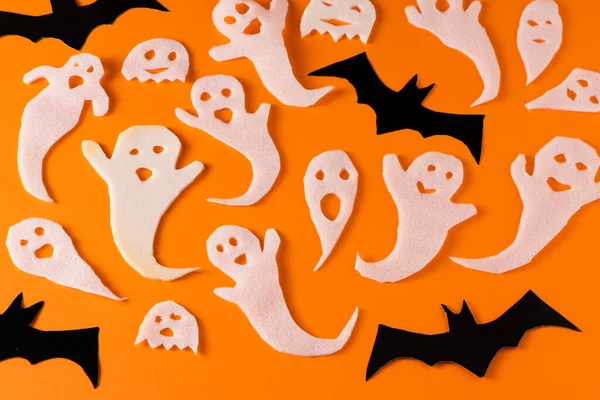 White ghosts and bat craft for Halloween party. Wrapping paper ghost on orange background top view. Cartoon creepy Whisper. DIY hand made. Set boo characters.
