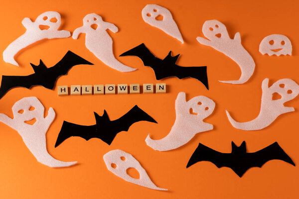 Белые призраки и летучая мышь для Хэллоуина. Обёртывание бумажным призраком на оранжевом фоне. Мультяшный жуткий шепот. Самодельная ручная работа. Установите символы буо. Слово деревянная буква.