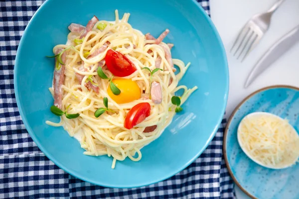 Peynirli ve yumurtalı makarna, pastırma ve domates, mikroyeşil. Mavi tabakta yemek. Ev yapımı carbonara makarnası. Öğle yemeği masanın üst tarafında. Jambonlu İtalyan spagettisi, krema.