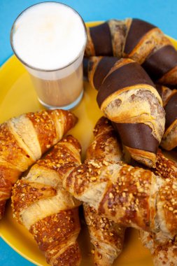 Çikolatalı kruvasan ya da üzerinde fındık kırıntıları olan kruvasan. Masada nefis bir kahvaltı. Kahve için lezzetli tatlı bir tatlı. Yemek arkaplanı. Taze tereyağlı kruvasanlar.