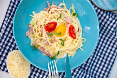 Peynirli ve yumurtalı makarna, pastırma ve domates, mikroyeşil. Mavi tabakta yemek. Ev yapımı carbonara makarnası. Öğle yemeği masanın üst tarafında. Jambonlu İtalyan spagettisi, krema.