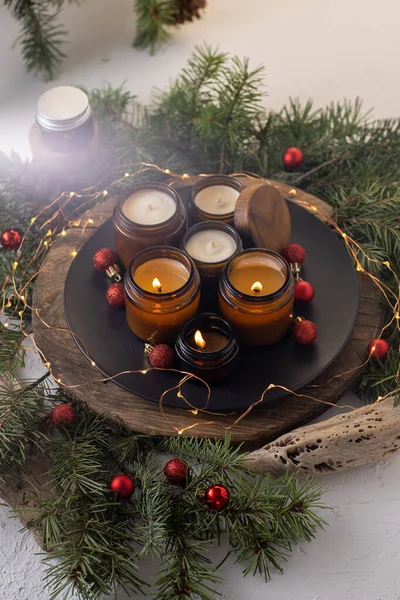 stock image Soy candles burn in glass jars. Comfort at home. Candle in a brown jar. Scent and light. Scented handmade candle. Aroma therapy. Christmas tree and winter mood. Cozy decor. Festive garland decoration