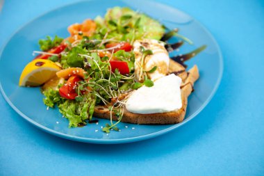 Sağlıklı kahvaltı. Avokado ve somon, haşlanmış yumurta ve tost, salata ve sebze. Tabakta mikroçimler. Yemek kasesi. Mavi tabakta öğle yemeği. Sos ve susam tohumları, limon domatesleri. Üst görünüm.