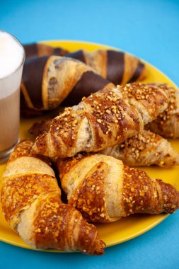 Çikolatalı kruvasan ya da üzerinde fındık kırıntıları olan kruvasan. Masada nefis bir kahvaltı. Kahve için lezzetli tatlı bir tatlı. Yemek arkaplanı. Taze tereyağlı kruvasanlar.