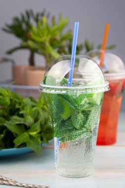 Naneli limon ferahlatıcı kokteyl mojito. Plastik bardakta buzlu ve samanlı. Karbonatlı maden suyu. İçki için bardak. Bar menüsünde limonata. Klasik köpüklü içecek.