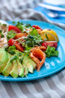 Sağlıklı kahvaltı. Avokado ve somon tostu, salata ve sebze. Tabakta mikroçimler. Yemek kasesi. Mavi tabakta öğle yemeği. Sos ve susam tohumları, limon domatesleri. Üst görünüm.