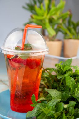 Naneli çilek ferahlatıcı kokteyl mojito. Plastik bardakta buzlu ve samanlı. Karbonatlı maden suyu. İçki için bardak. Bar menüsünde limonata. Klasik köpüklü içecek.