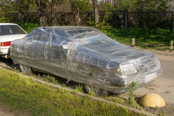 stock image The passenger car is packed in a plastic bag made of stretch film and stands on the street. Storage is an alternative to a garage. Vandalism and revenge. Disposal of packaging. Humor