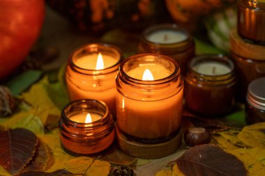 Soya mumları cam kavanozlarda yanar. Ağaç yaprakları. Evdeki rahatlık. Kahverengi kavanozdaki mum. Koku ve ışık. Kokulu el yapımı mum. Aroma terapisi. Sonbahar havası. Sonbaharda ev dekorasyonu. Şenlikli dekorasyon.