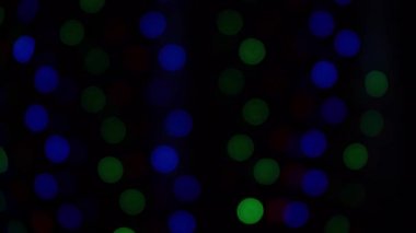 Bokeh çelenkleri yakıyor. Bulanık yumuşak odak. Çelenk yanıp sönüyor. Gece şehir ışıkları. Aralık 'ta Noel havası. Kışın ev penceresi. Siyah arkaplanda çok renkli ışık 4K görüntüsü.