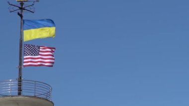 Ukrayna ve ABD 'nin bayrakları mavi gökyüzüne karşı bir bayrak direğinde dalgalanıyor. Devlet sembolü. Ukrayna mavi ve sarı bayrağı. Rüzgar açık havada eser..