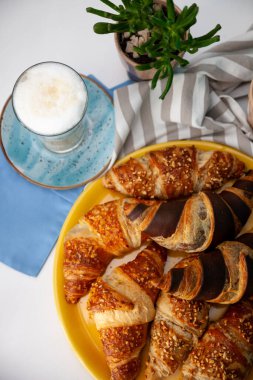 Çikolatalı kruvasan ya da üzerinde fındık kırıntıları olan kruvasan. Masada nefis bir kahvaltı. Kahve için lezzetli tatlı bir tatlı. Yemek arkaplanı. Taze tereyağlı kruvasanlar.