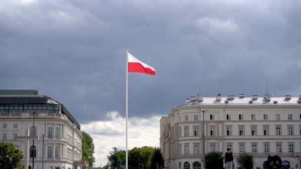 波兰国旗在蓝天的风中飘扬 乌云中闪烁着波兰的红白国旗 广场上的旗杆 街上的房子 — 图库视频影像
