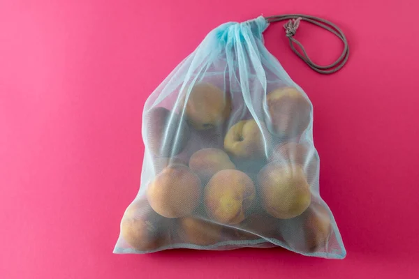 Eco bag for shopping in the store. Mesh replacement for plastic bag. Eco-friendly concept background. Zero waste. Peach fruits in bag.