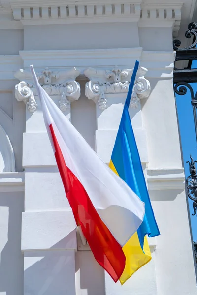 The flags of Ukraine and Poland flutter in the wind. Support and friendship of countries. Waving flag on the street close up.