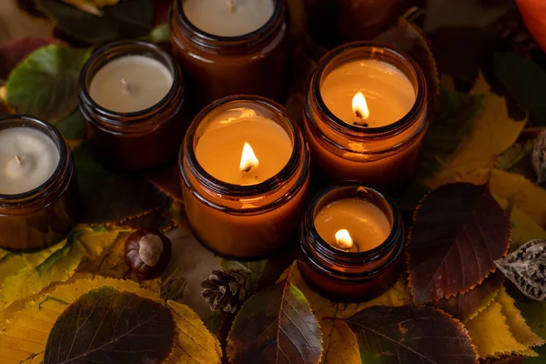 Soy candles burn in glass jars. Tree leaves. Comfort at home. Candle in a brown jar. Scent and light. Scented handmade candle. Aroma therapy. Autumn mood. Cozy home decor in fall. Festive decoration.