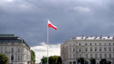 Mavi gökyüzünde rüzgarda dalgalanan Polonya bayrağı. Bulutlarda Lehçe beyaz kırmızı bayrak. Meydanda bayrak direği. Sokaktaki evler..