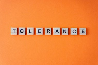 Tolerance word. The phrase is laid out in wooden letters top view. Orange flat lay background clipart