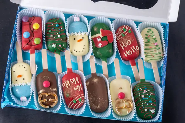 Christmas dessert. Sweet food. Cheesecake on a stick in the shape of ice cream. Childrens treat in winter. Candy Christmas tree, snowman, deer and Santa Claus. Gingerbread cookies in gift box