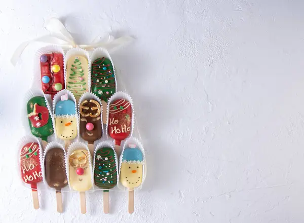 Christmas dessert. Sweet food. Cheesecake on a stick in the shape of ice cream. Childrens treat in winter. Candy Christmas tree, snowman, deer and Santa Claus. Gingerbread cookies. White background.